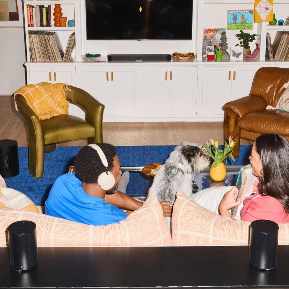Two people sitting on a couch with a dog and a black Beam Ultra soundbar in a modern living room
